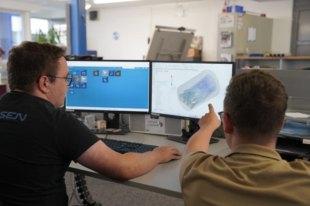 Zwei Mitarbeiter von Jansen sehen gemeinsam auf einen PC Monitor auf dem eine visuallisuerung einer CFS Flow Analyse gezeigt wird.